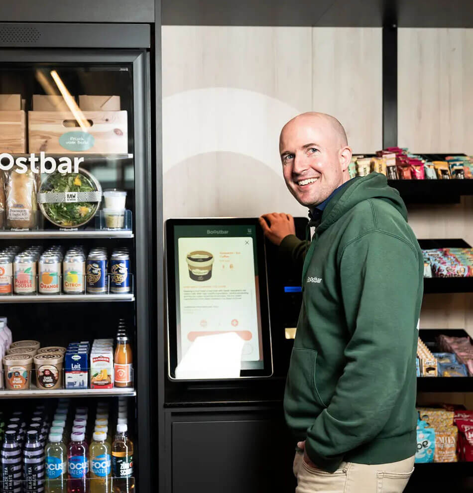 Man stood smiling with vending machine and self checkouts